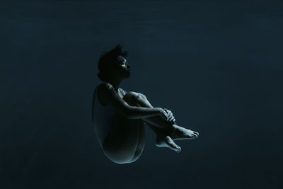 Young woman in fetal position swimming underwater