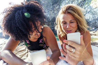 Smiling two women taking selfie while lying on rock formation at sea