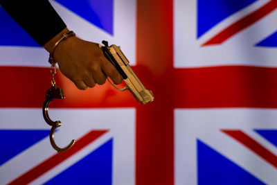 Cropped hand of male criminal holding gun against british flag