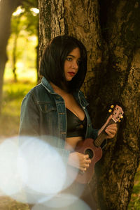 Portrait of young woman with guitar on tree trunk