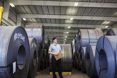 Supervisor standing amidst rolled up metal sheets in storage room