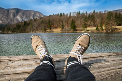 Low section of person relaxing by lake against sky