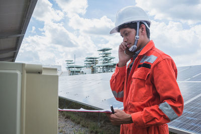 Side view of worker talking on phone while standing by solar panel