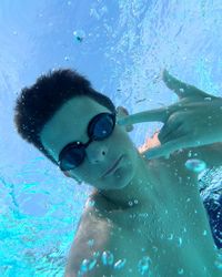 Portrait of teenage boy gesturing horn sign while swimming in pool