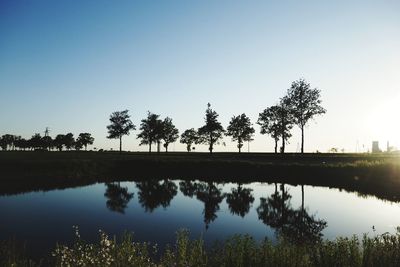 Silhouette trees by lake against clear sky during sunset