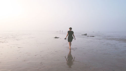 Rear view of man walking on beach against clear sky