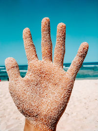 Close-up of hand on sand at beach against sky