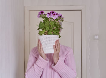 Midsection of person holding pink flower against wall