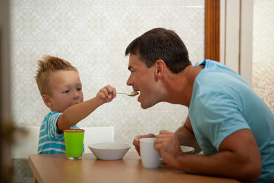 Cute son feeding food to father at home