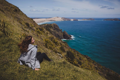 Woman sitting by sea against sky