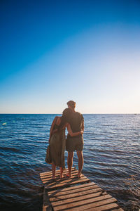 Rear view of man standing on pier over sea against sky