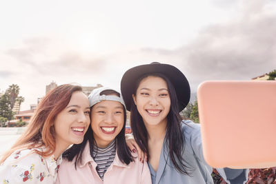 Portrait of smiling young woman using smart phone against sky