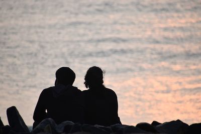 Rear view of couple sitting against sky during sunset