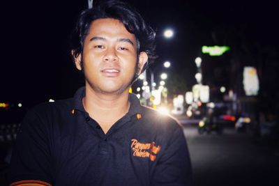Portrait of smiling young man standing in city at night