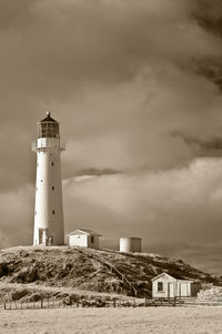Lighthouse on hill against cloudy sky