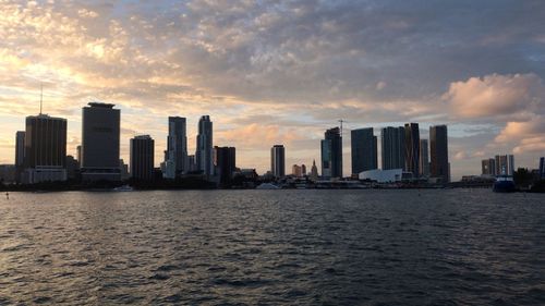 Sea by city buildings against sky during sunset