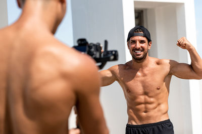 Smiling shirtless man flexing muscle while looking at friend