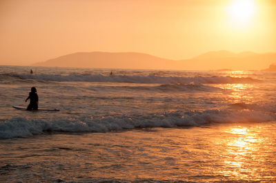 Silhouette man standing in sea against sky during sunset