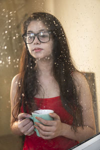 Young woman holding coffee cup seen through mirror