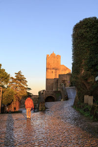 Rear view of woman walking by historic building against clear sky