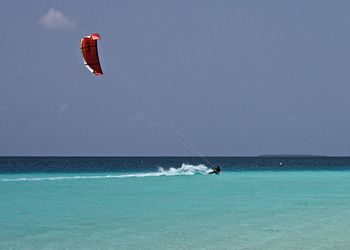 Person paragliding in sea against clear sky