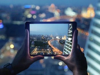 Cropped hand of man photographing city through digital tablet