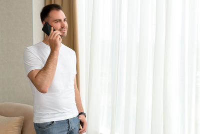 Man talking on phone while standing by window