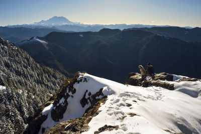 High angle view of man sitting with dog on snowcapped mountain