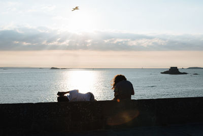 People on retaining wall against sea during sunset