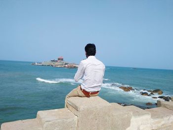 Rear view of man looking at sea against clear sky