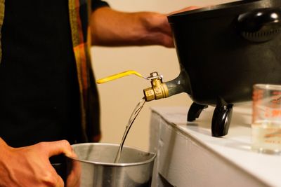 Midsection of person pouring liquid wax in pitcher