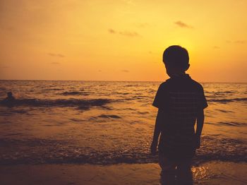 Silhouette boy standing at beach during sunset