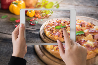 Cropped hands of woman photographing pizza with digital tablet on wooden table