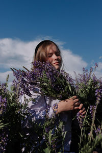 Caucasian young woman with bouquet of purple flowers in field
