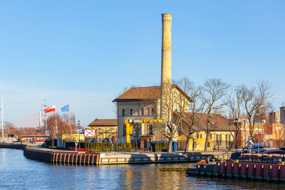 Buildings by river against clear sky