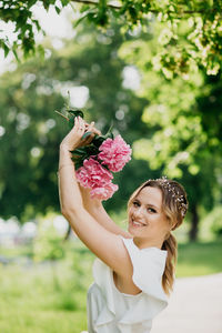 Portrait of young woman holding flower against plants