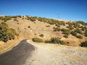 Scenic view of road amidst trees against clear blue sky