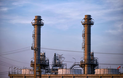 Communications tower in factory against sky