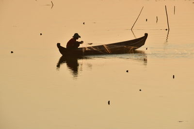 Man in boat on lake against sky during sunset