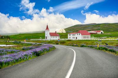The curved road leads to the church of kopasker. the white church has a red roof in an icelandic 