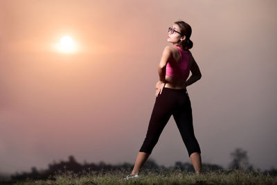 Full length of woman exercising on field against sky during sunset