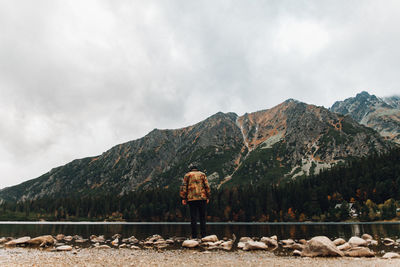 Rear view of man standing by lake against sky