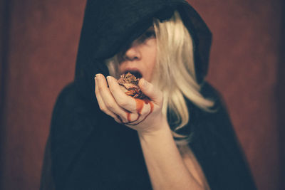 Portrait of witch eating dry flower against wall at home