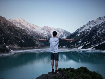 Rear view of man standing on rock by lake against sky