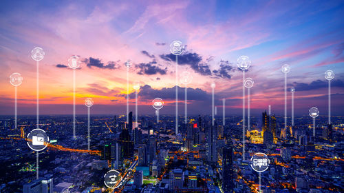 Digital composite image of illuminated buildings against sky during sunset