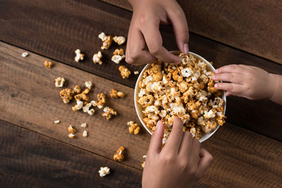 Cropped hands having popcorns in bowl on wooden table