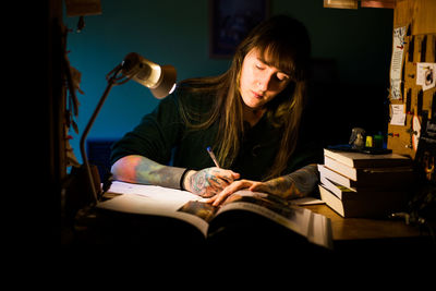 Young woman writing in book sitting at home