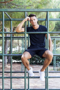 Portrait of man sitting on metal structure in playground