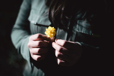 Midsection of woman holding flower in darkroom