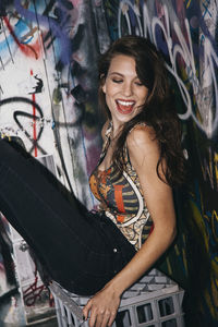 Smiling young woman sitting while leaning against wall